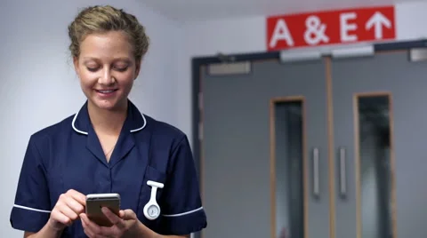 Smiling nurse using cell mobile phone in front of doors in hospital  스톡 동영상 59087316