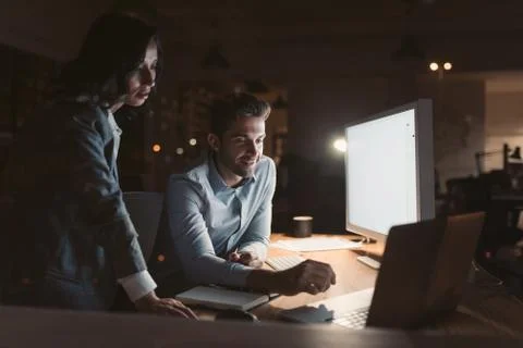 Smiling office colleagues working on a computer together at night Stock Photos