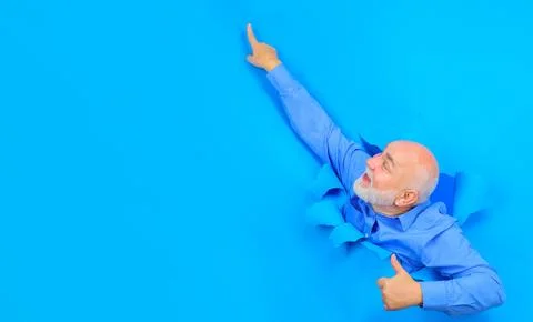 Smiling old bearded man looking through hole in paper showing thumb up. Senio Stock Photos