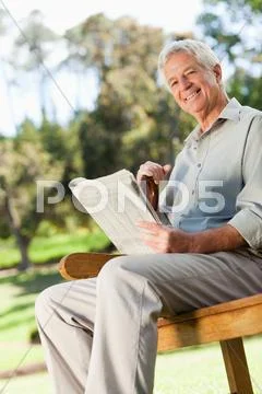 Smiling Old Man Holding A Newspaper Is Sitting Down