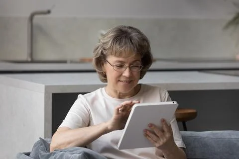 Smiling older lady using tablet computer, sitting on couch Stock Photos