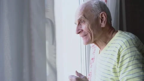 Smiling older man looking through window glass and waving greeting gesture. Stock Footage 164436894
