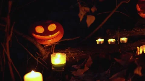 Smiling orange spooky glowing carved pumpkin among white burning candles outside Stock Footage 139199853