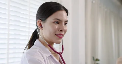 Smiling pediatrician using a red stethoscope in a bright hospital room. Stock Footage 297547721