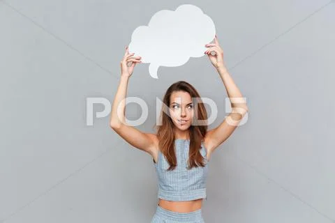 Smiling pensive young woman thinking and holding empty speech bubble Stock Photos