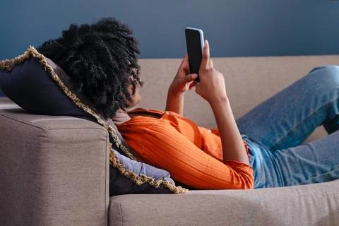 Smiling person using mobile phone on comfortable sofa in modern interior setting Stock Photos