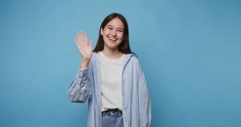 Smiling person waves hello in a studio with a blue background during the day 動画素材 328248341