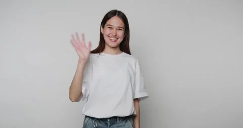 Smiling person waves hello in studio against a light background in a friend.. 스톡 동영상 328248489