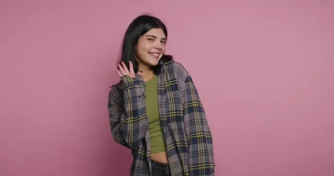 Smiling person waves while wearing a large checkered shirt in front of a pi.. Vídeos de archivo 326792377