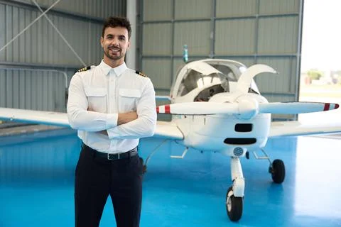 Smiling pilot posing with arms crossed in front of small airplane Stock Photos