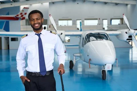 Smiling pilot posing with suitcase in aircraft hangar Stock Photos