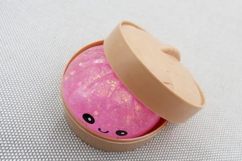 Smiling pink glitter dumpling squishy toy presented in a natural bamboo bowl Foto stock