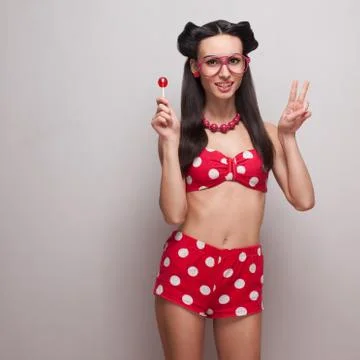 Smiling pinup model posing with red candy and showing peace Foto stock