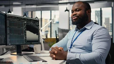 Smiling portfolio manager at computer desk evaluates assets based on statistics Stock-Fotos