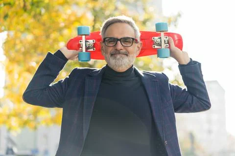 A smiling, positive, bearded, grey-haired mature man with glasses on, holding a Stock Photos