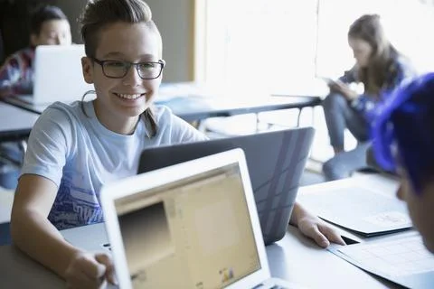 Smiling pre-adolescent boy programming at laptop in classroom Stock Photos
