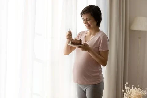 Smiling pregnant woman eat chocolate cake at home Stock Photos