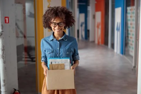 Smiling pretty lady posing while carrying a box of documents in the office Stock Photos