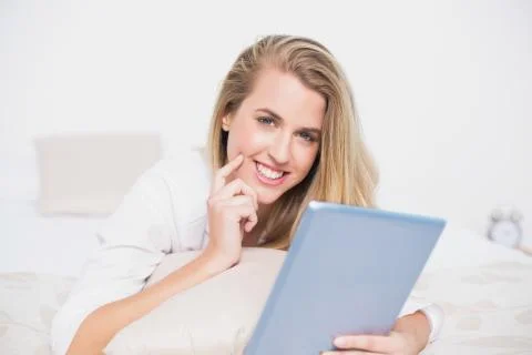 Smiling pretty model using her tablet lying on cosy bed Stock Photos