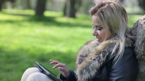 Smiling pretty woman using tablet sitting under a tree Video stock 74710687