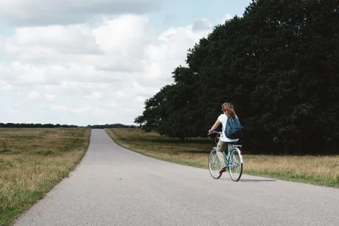 Smiling pretty young woman riding bike in a country road in the park Stock Photos