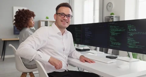 Smiling programmer coding at multi monitor setup in modern office with Stock Footage 341295077
