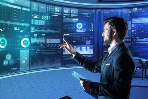 Smiling programmer holding a transparent tablet and pointing to a screen Stock-Fotos