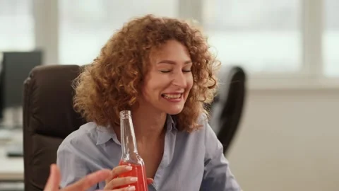 A smiling red-haired lady sits in a circle of her colleagues and drinks a low Stock Footage 243257399