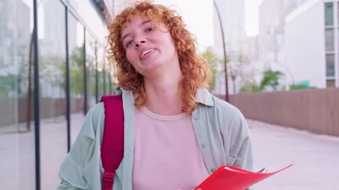 Smiling red-haired student with backpack and books looking at camera outdoors Stock Footage 295198727