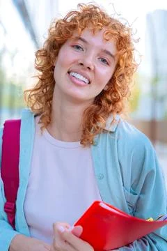 Smiling red-haired student with backpack and books outdoors.Vertical Foto stock