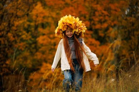 Smiling redhead girl in a massive maple leaf wreath walking on a grassy hil.. Foto stock