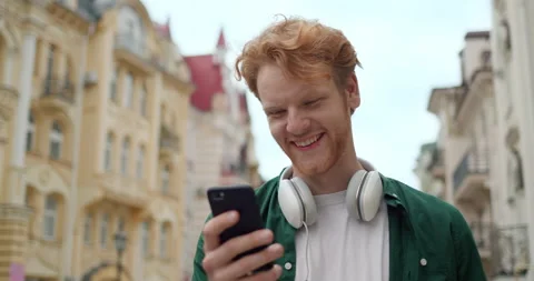 Smiling Redhead Hipster Guy standing outdoors Looking at Phone Screen. Uses Stock-Footage 157556963