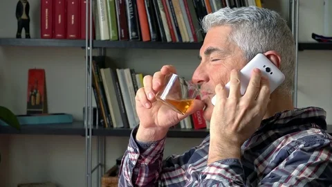 Smiling relaxed mature man drinking whisky while having a phone call  Vídeo Stock 73168053