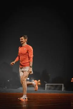 Smiling runner mid stride on a damp track at night Stock Photos