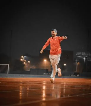 Smiling runner pointing ahead on a damp track at night Stock Photos
