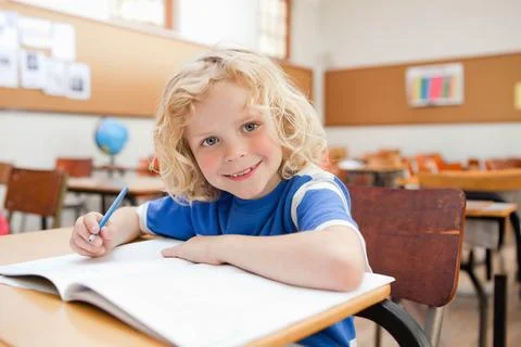 Smiling schoolboy sitting at desk with exercise book Stock Photos
