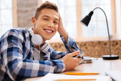 Smiling schoolboy sitting at the table with his phone Stock Photos