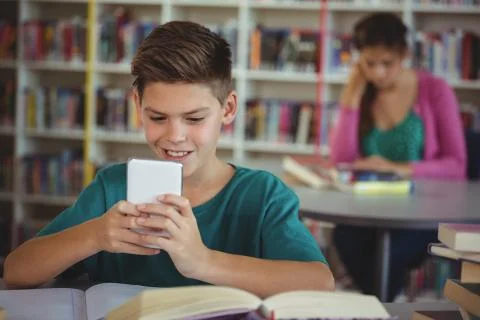 Smiling schoolboy using mobile phone in library Stock Photos