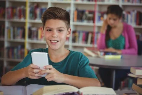 Smiling schoolboy using mobile phone in library at school Foto stock