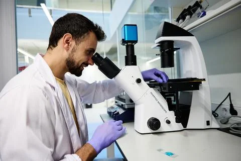 Smiling scientist examining a sample under an inverted microscope in a lab Фото