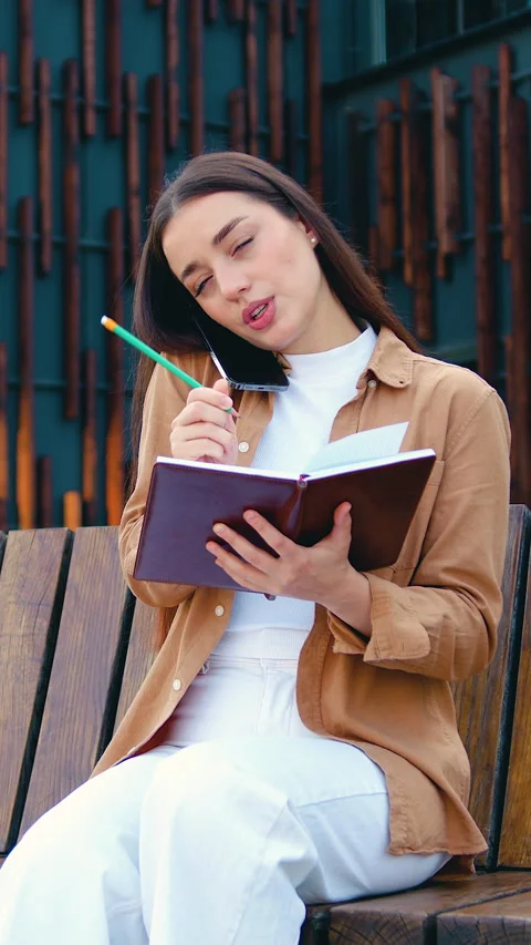 Smiling self employed female making phone call on mobile phone and taking notes  Stock Footage 327547873