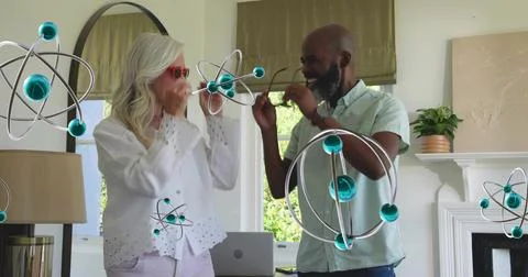 Smiling senior couple interacting with floating atom models at home, with laptop Stock Photos