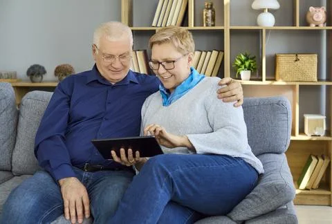 Smiling senior couple using digital tablet together at home on a comfortable Stock Photos
