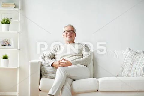 Smiling senior man in glasses sitting on sofa Stock Photos