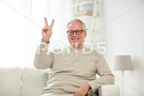 Smiling senior man showing v sign at home Stock Photos