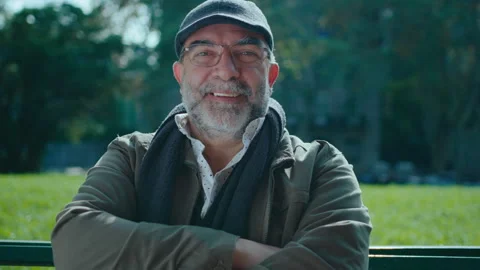 Smiling Senior Man Sitting on Bench in the Park and Posing for Camera Stock Footage 245395723