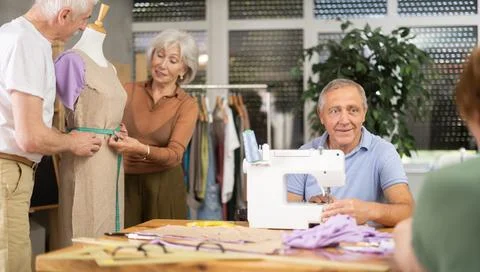 Smiling senior man stitching at machine during group class Foto stock