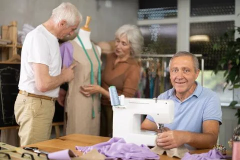 Smiling senior man stitching at machine during group class Foto stock