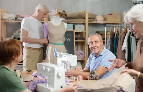 Smiling senior man stitching at machine during group class Foto stock