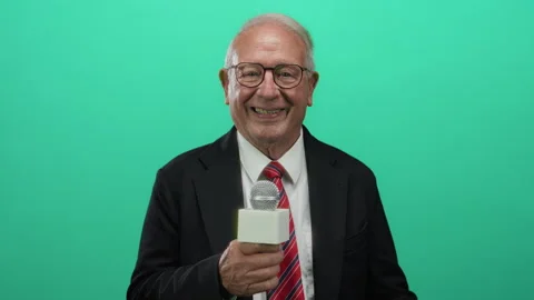 Smiling senior man in a suit holding a microphone against a green backgroun.. Stock Footage 310998524